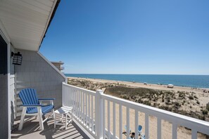 Un balcon donnant sur la plage, agrémenté d’une balustrade blanche, de deux fauteuils Adirondack bleus et d’une petite table.