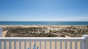 A beach view from a balcony with a white railing, sandy beach, and ocean. - Beautiful, modern, 4 bedroom oceanfront townhome! (Ocean City)