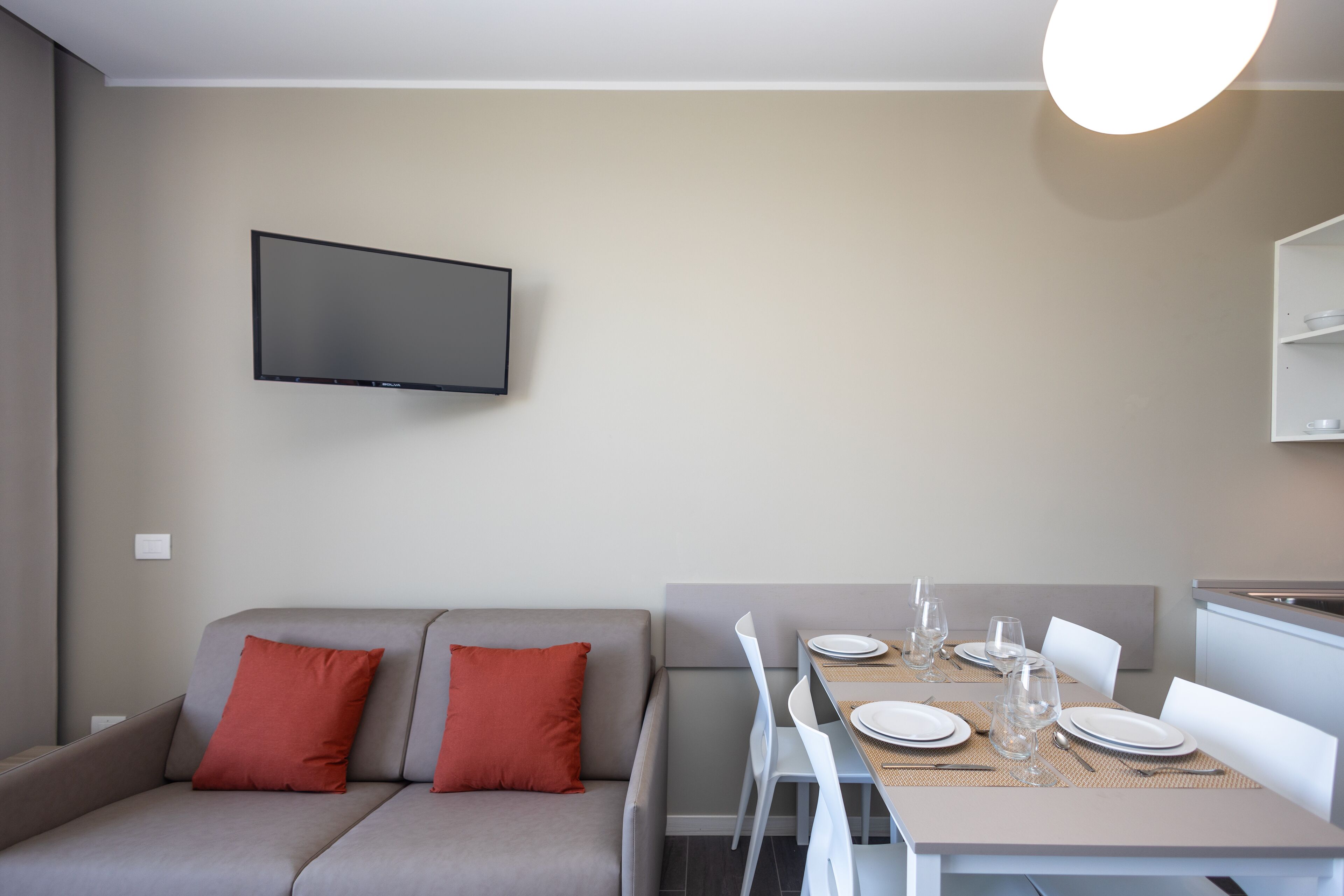 Un soggiorno moderno con un divano, un tavolo da pranzo apparecchiato per due persone e un televisore piatto montato a parete.