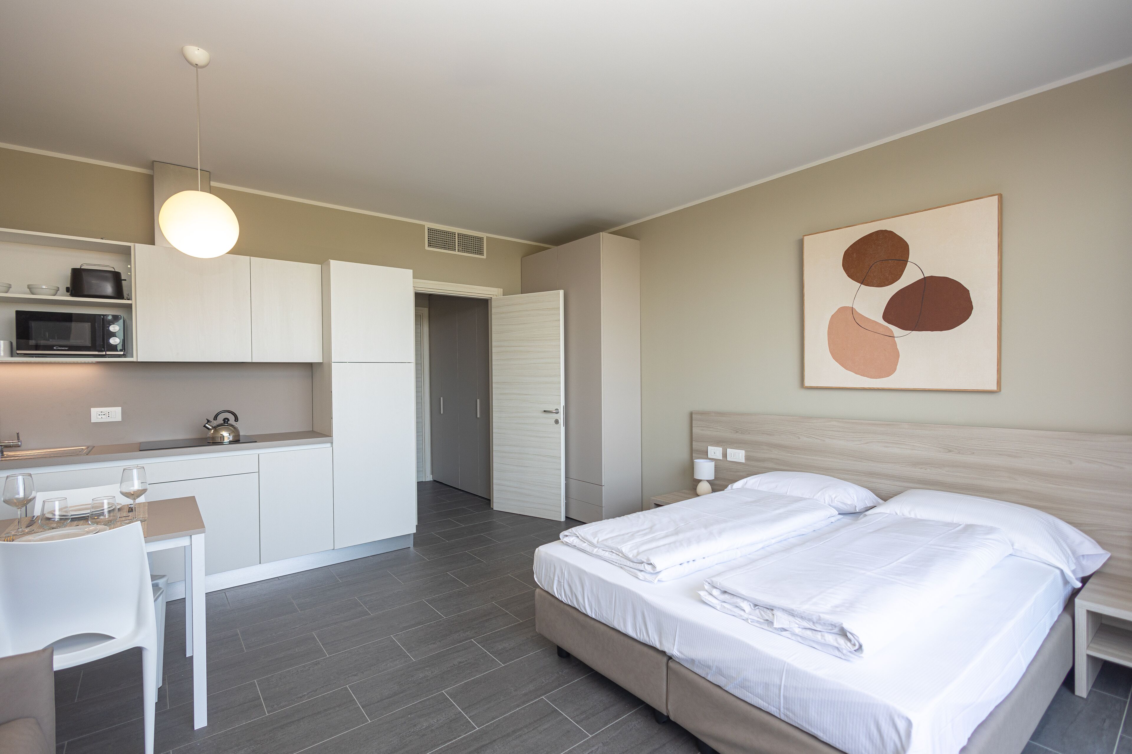 Une chambre d’hôtel moderne équipée d’un lit, de tables de chevet, d’un bureau avec une chaise, d’un four à micro-ondes et d’une kitchenette.
