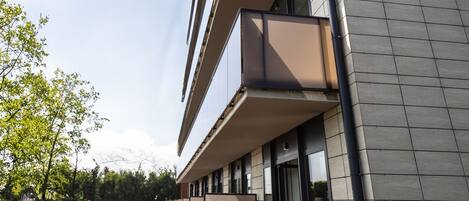 A modern building with multiple balconies, a flat roof, and a paved walkway.