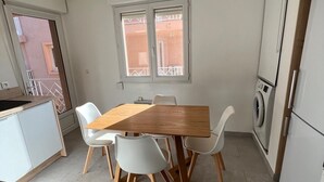A compact kitchen with a wooden dining table, white chairs, a washing machine, and a small window. - Très bel Appartement de 71 m², vue sur mer 250 m de la Plage ,du Centre-ville (L'Île-Rousse)