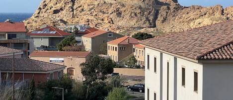 A coastal town with buildings, a prominent rocky hill, and a lighthouse.