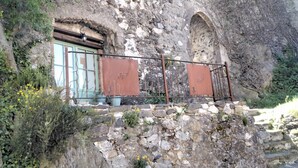 Ein rustikales Steinhaus mit einem Metallbalkon, einem kleinen Fenster und einer Steinmauer.