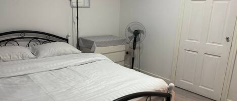 A bedroom with a bed, a bedside table, a lamp, a fan, and a door.