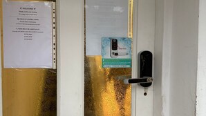 A door with a frosted glass panel, a brass door handle, and a keyhole. There is a sign with check-in instructions and a contact number for assistance. - Baraka House Royal Victoria London by OYO (London)
