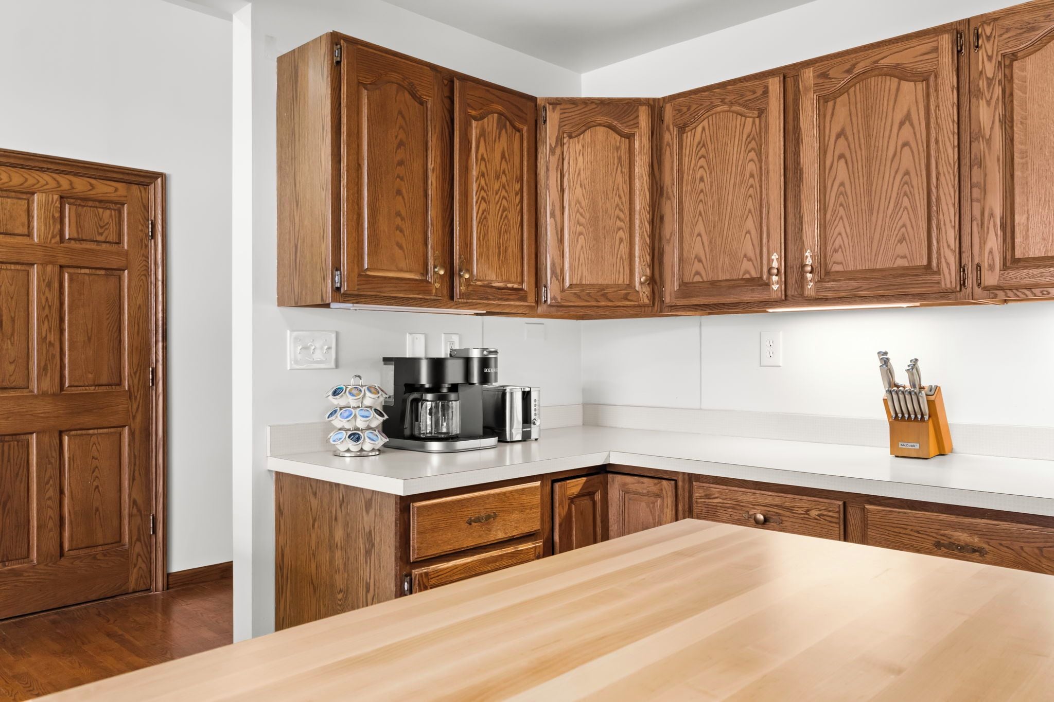 A kitchen with wooden cabinets, a countertop, a coffee maker, and a knife block.