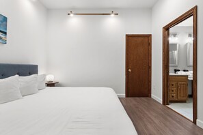 A bedroom with a bed, bedside table, nightstand, wooden door, and a mirror.