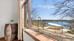 Een kamer met een groot raam met uitzicht op een meer, een houten vat en een kleine potplant.