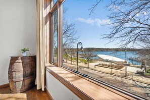 A room with a large window overlooking a lakeside view, a wooden barrel, and a potted plant. - Loft above the Villager Pub with Round Lake marina sunsets — walk Bridge St + East Park. (Charlevoix)