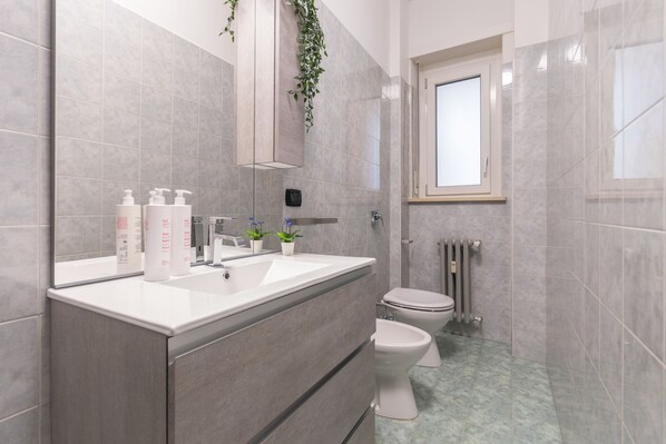 A modern bathroom with a large mirror, white sink, two toilets, and a radiator.