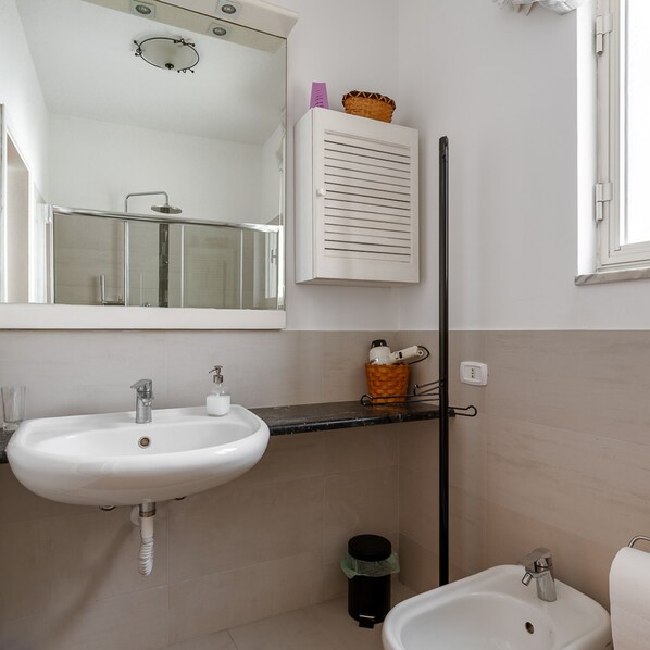 A bathroom with a white sink, a mirror, a towel rack, a bidet, and a small trash bin.