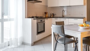 A modern kitchen with white cabinets, a gas stove, an oven, and a dining area with a table and chairs. - Syracuse Comfy Retreat by Wonderful Italy (Syracuse)