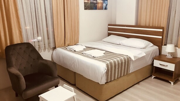 Et pænt indrettet hotelværelse med seng, stol, lille bord og et natbord med lampe.