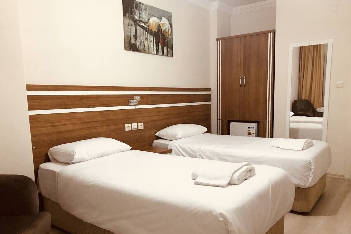 Quarto de hotel com duas camas, cabeceira de madeira, um quadro, guarda-roupa e um espelho.