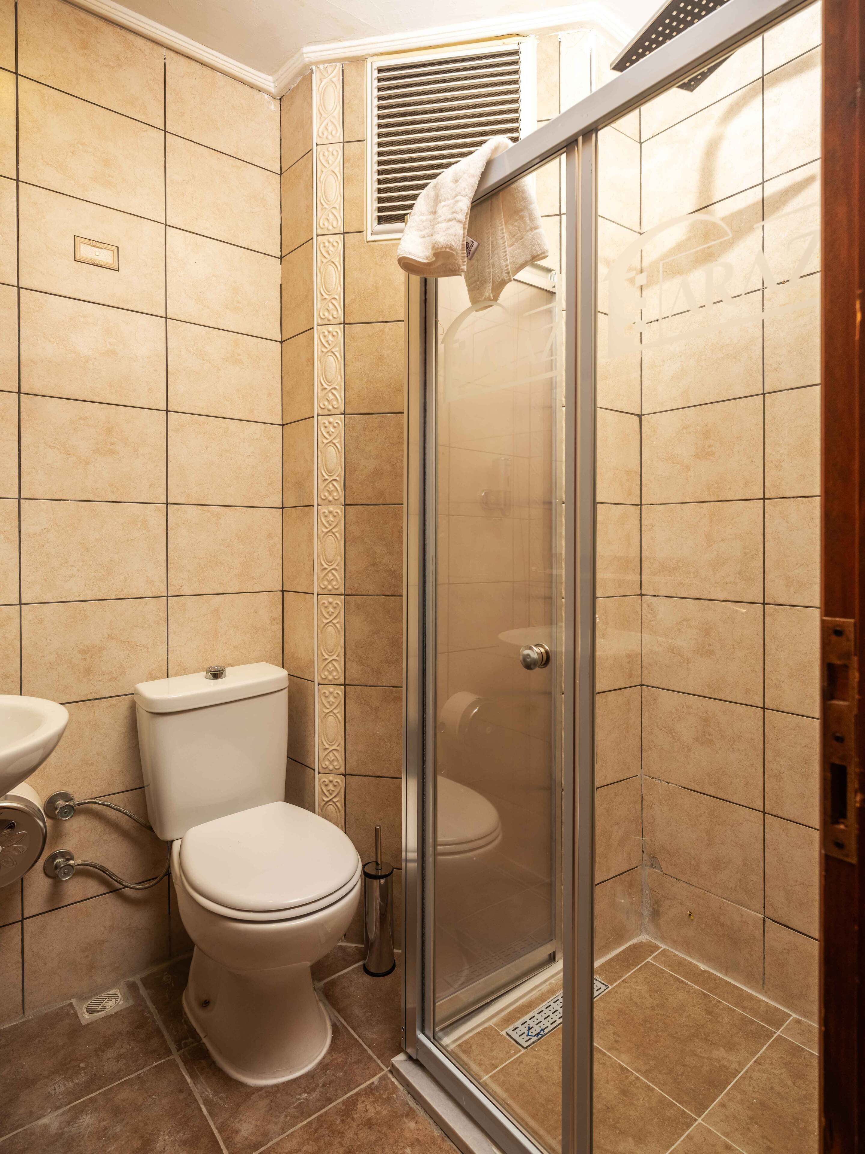 A bathroom with a toilet, a shower with a glass door, and a towel hanging on the shower door.