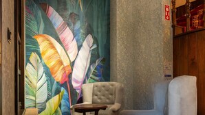 A room with a large tropical leaf mural, a tufted armchair, a small round table, and a wooden bench. - Araz White House (Mudanya)