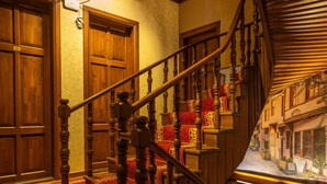 A grand staircase with ornate wooden balusters and red carpeted steps leading to a landing with a view of a street scene. - Araz White House (Mudanya)