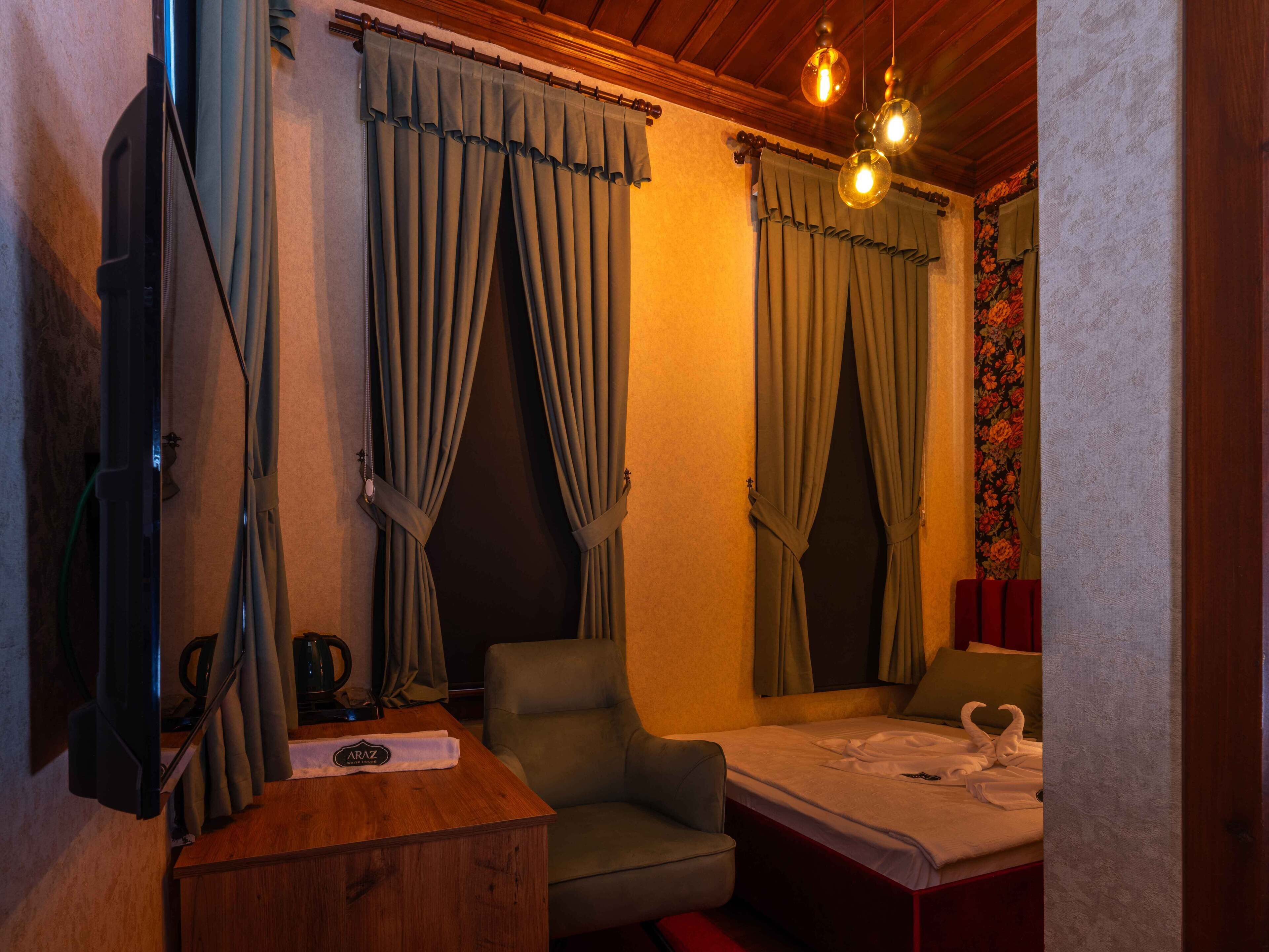 Une chambre d’hôtel avec un bureau en bois, une chaise, un lit recouvert d’une courtepointe blanche et doté de serviettes, ainsi que des rideaux.