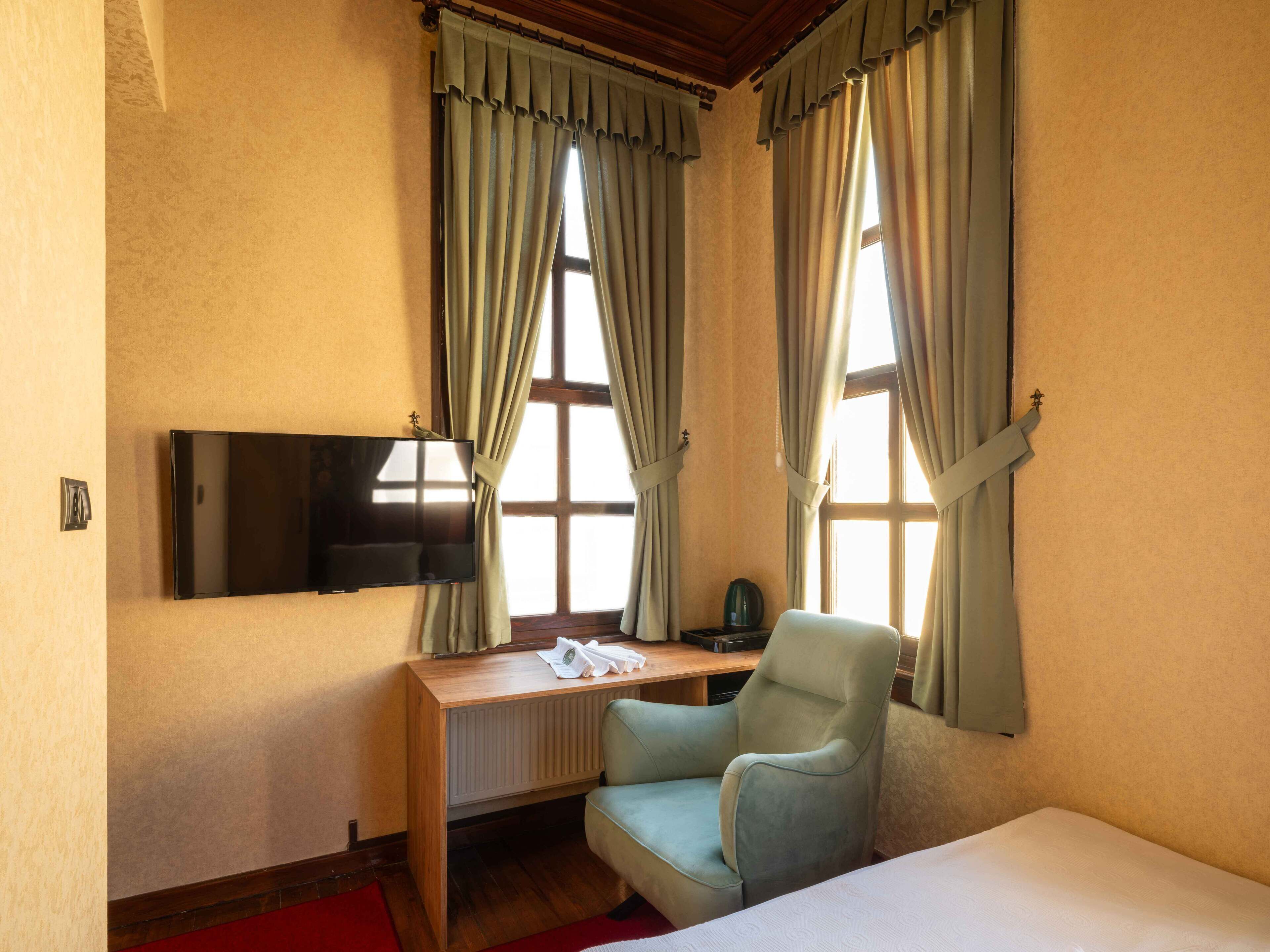 Una habitación de hotel con una cama, un escritorio con una silla, un televisor y dos ventanas con cortinas.
