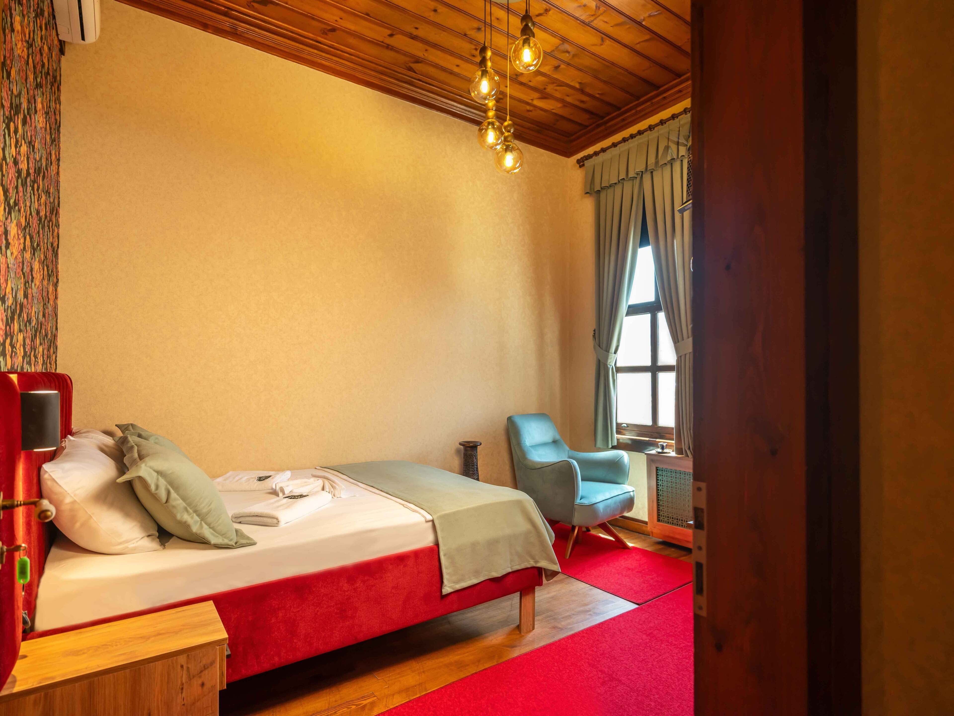Un dormitorio con cama, una silla, un ventanal y una lámpara en el techo.