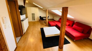 Ein kompakter Wohnraum mit Küchenzeile, einem roten Sofa, einem weißen Couchtisch und einem Oberlicht.