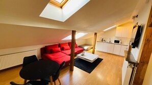 Ein kompakter Wohnraum mit Essbereich, einem roten Sofa, einer Küche und einem Oberlicht.