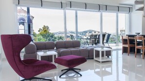 A modern living room with a large window, a sofa set, a purple chair, and a dining area.