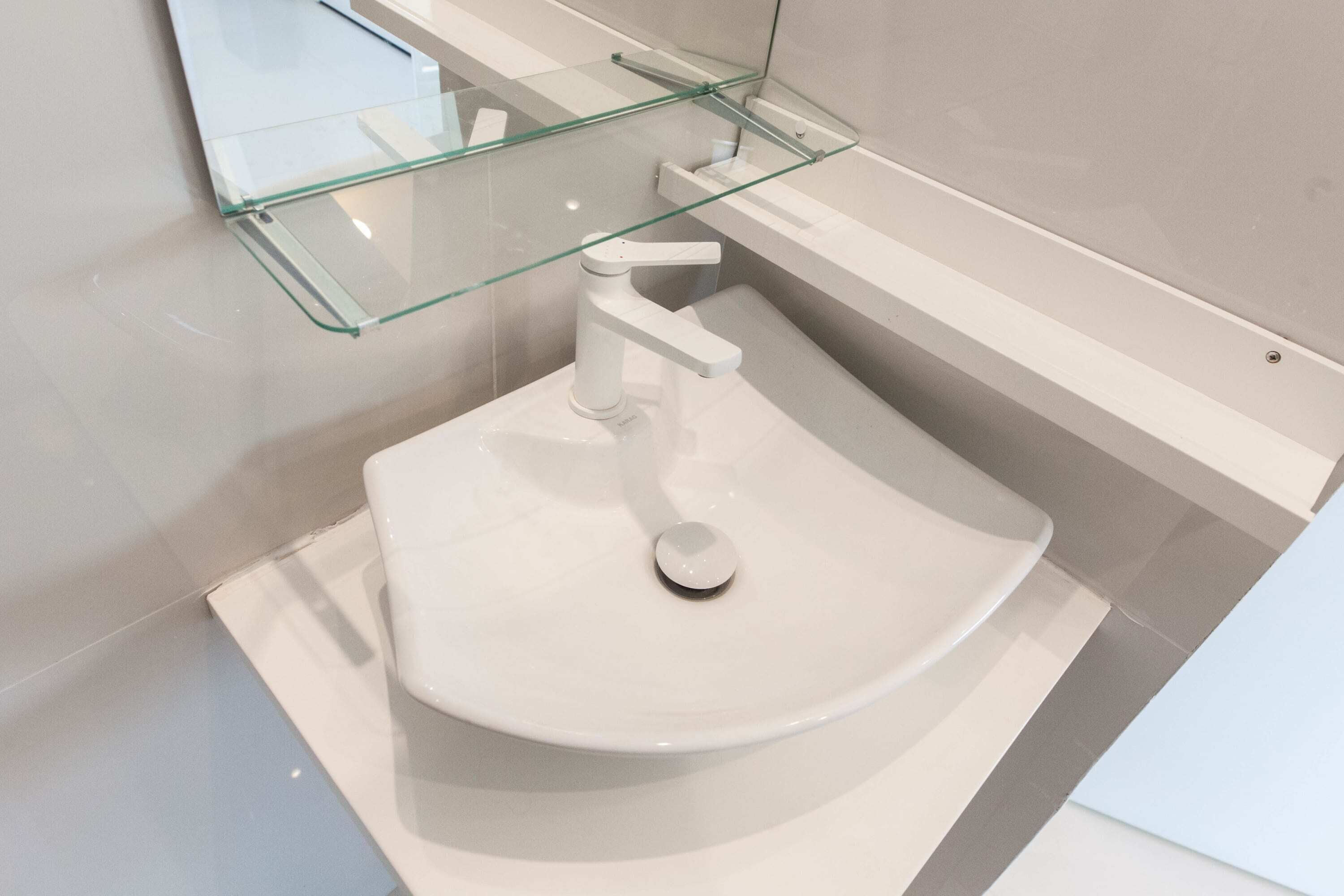 Une salle de bain moderne avec un lavabo blanc, une étagère en verre et un miroir.