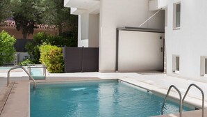 A rectangular swimming pool with metal railings, surrounded by a tiled deck and a low wall.