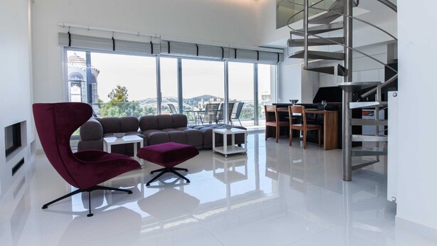 A modern living room with a large window, a red chair, a sofa, and a spiral staircase.