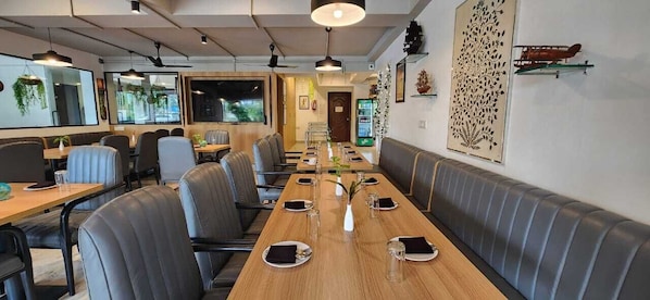 A restaurant with long wooden tables, cushioned booths, and hanging plants.