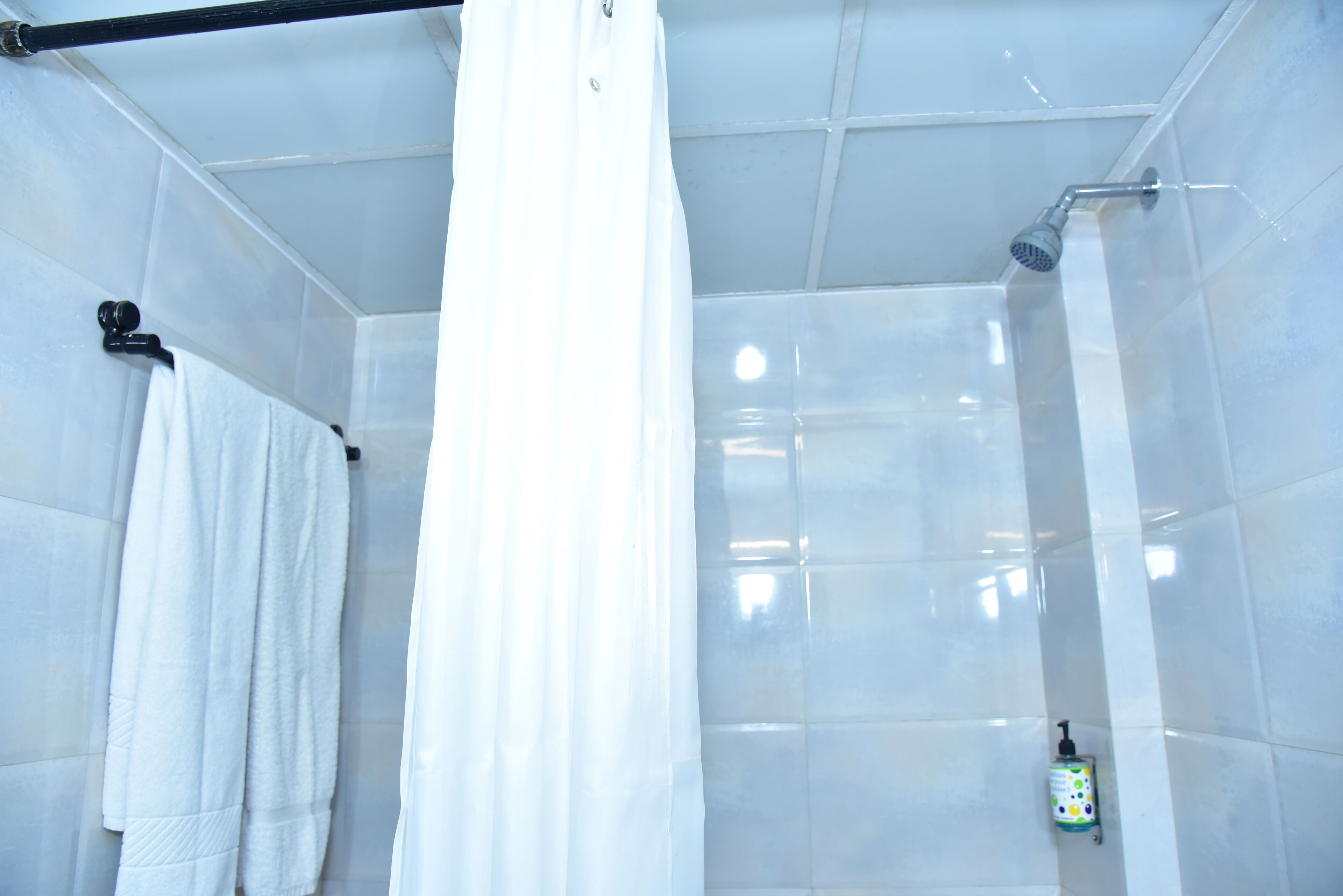 A bathroom with white tiled walls, a shower with a handheld showerhead, and a white towel hanging on a rack.
