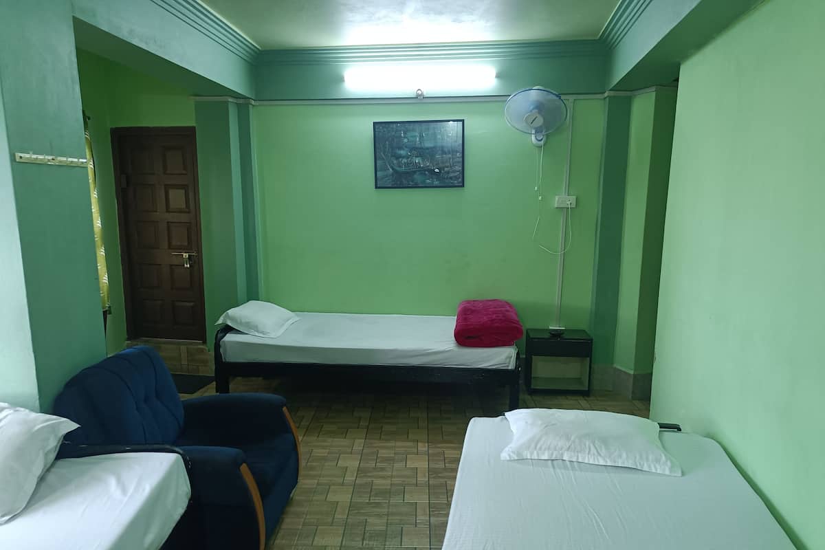A room with two beds, a chair, a fan, and a door.