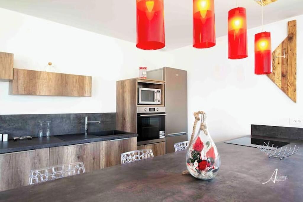 Een moderne keuken met een centraal eiland, roestvrijstalen apparatuur en rode hanglampen.