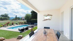 A modern patio with a wooden table and chairs, a pool, and a view of a lush garden and mountains. - Villa Pardisoli 2. Logement Entier : Hébergement - Prunelli-di-fiumorbo, France (Prunelli-di-Fiumorbo)