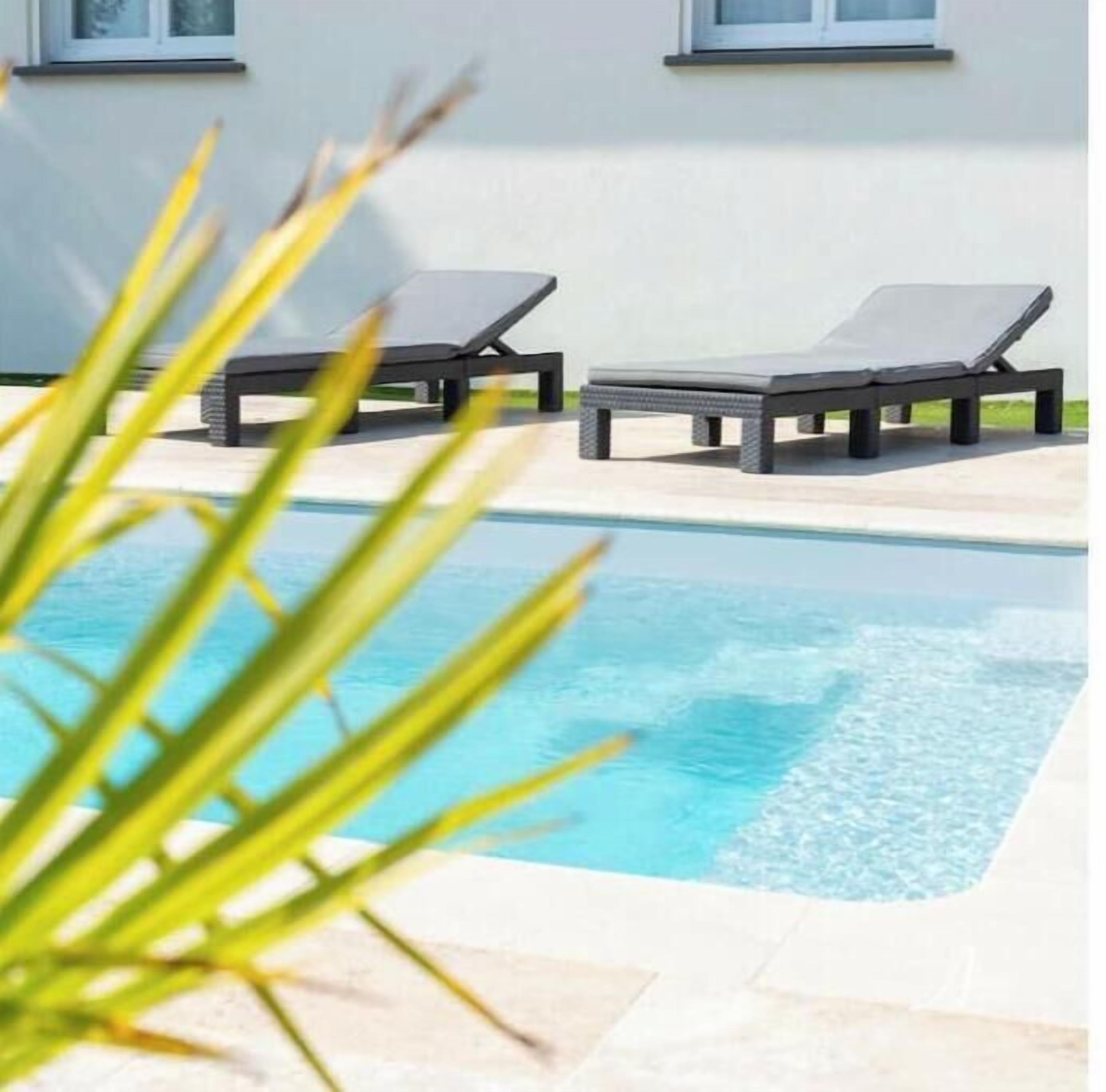 Una piscina con dos sillas de descanso y un edificio al fondo.