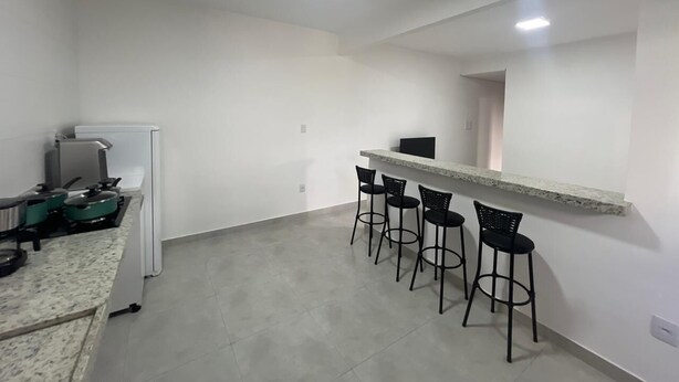 A kitchen with a gas stove, a refrigerator, and a bar area with four stools.