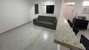A spacious living area with a grey sofa, a kitchen counter, and a dining area.