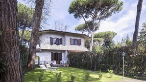 A two-story house with a garden, a patio with outdoor furniture, and a large tree in the background. - Wonderful  villa for 5 people with WIFI, A/C, TV, terrace and pets allowed, close to Forte Dei M... (Marina Dei Ronchi)