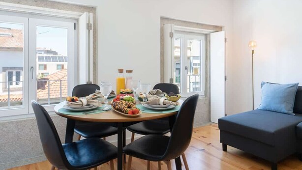 Un comedor con una mesa lista para cuatro personas, un sofá y vistas de la ciudad a través de amplios ventanales.