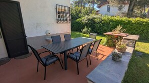 An outdoor patio with a table and chairs, a wall-mounted light fixture, and a garden area with a potted plant. - Stunning private villa for 8 guests with A/C, WIFI, TV and pets allowed, close to Forte Dei Marmi (Marina Dei Ronchi)