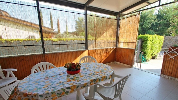 Un patio techado con mesa y sillas, un cerco de madera y vistas al exterior.