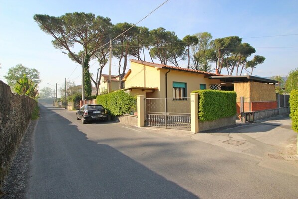 A residential street with a house featuring a tiled roof, a gated entrance, and a parked car.