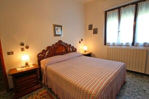 A bedroom with a wooden bed, two bedside tables with lamps, a radiator, and a window with curtains.