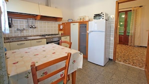 Cocina compacta con estufa, lavamanos y refrigerador. Hay una mesa de comedor con sillas. La cocina tiene un salpicadero de azulejos y un reloj en la pared.