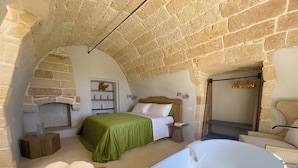 Une chambre avec une cheminée en pierre, une grande baignoire et un lit avec une literie verte.