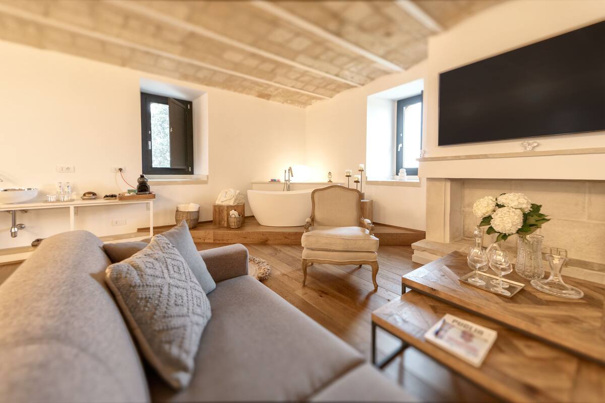 Un salon moderne comprenant un canapé, un fauteuil, une table basse en bois, une cheminée et un grand téléviseur à écran plat fixé au mur.