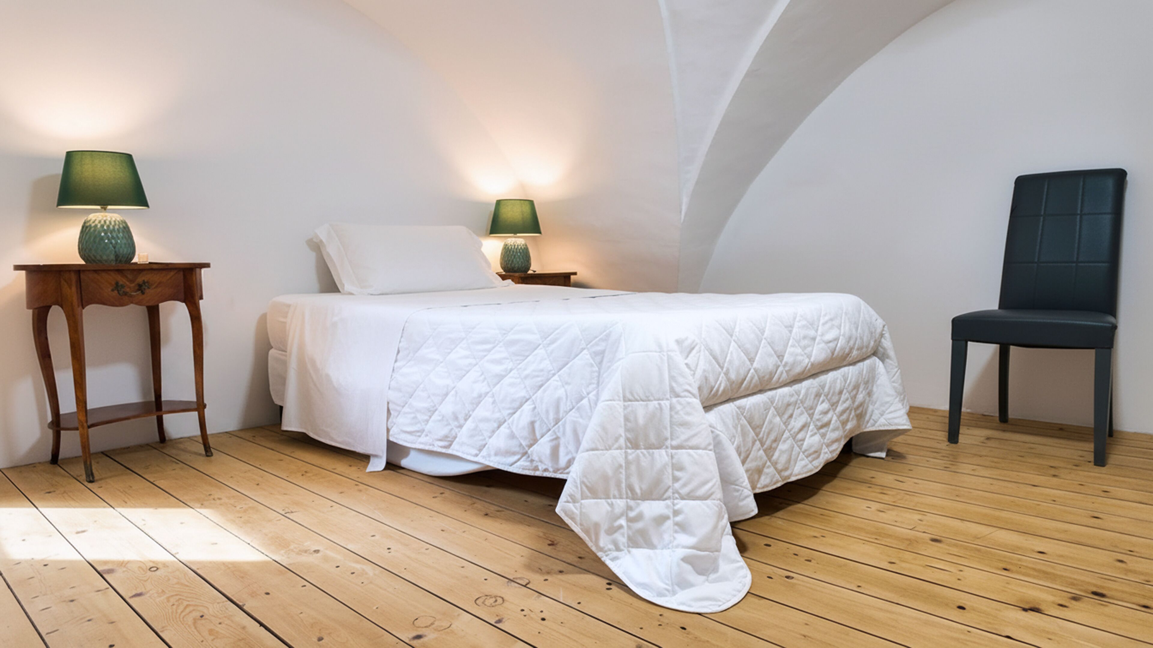 Una camera da letto con un letto, due comodini, una sedia e pavimento in legno.