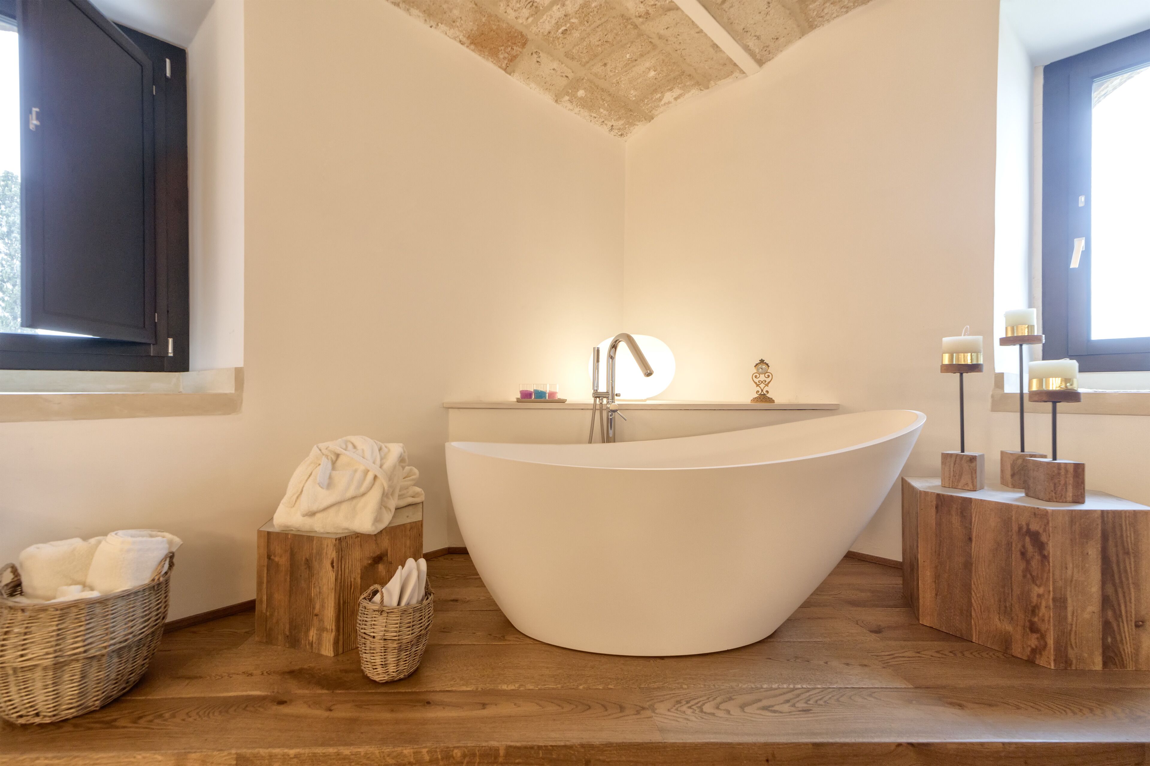 Une salle de bain moderne avec une baignoire sur pieds, des tables d’appoint en bois et une fenêtre laissant entrer la lumière naturelle.